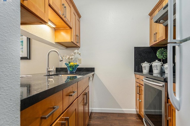 kitchen featuring stainless steel range with electric cooktop, decorative backsplash, fridge, dark stone countertops, and sink