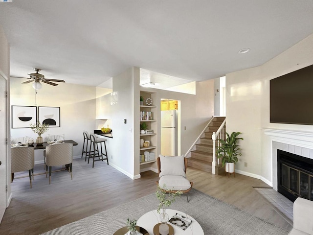 living room featuring hardwood / wood-style flooring, lofted ceiling, built in shelves, a tiled fireplace, and ceiling fan