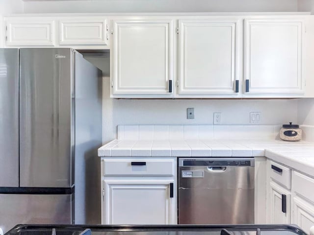 kitchen featuring appliances with stainless steel finishes, tile counters, and white cabinets