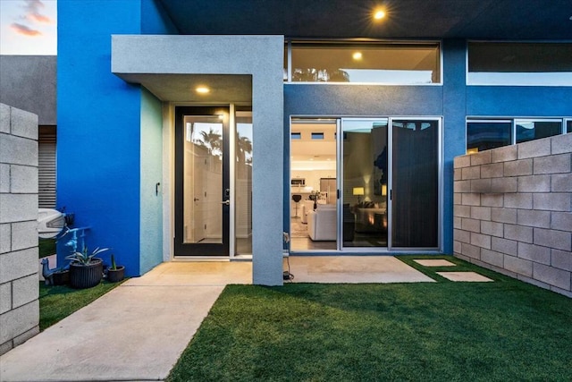 view of exterior entry featuring a lawn and a patio area