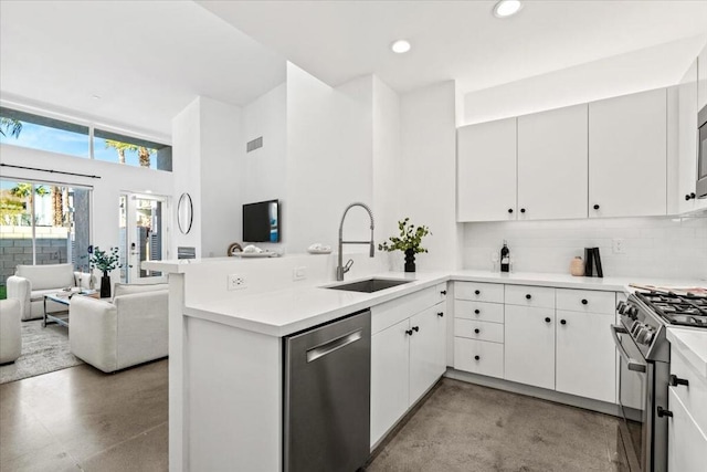 kitchen with appliances with stainless steel finishes, white cabinetry, decorative backsplash, sink, and kitchen peninsula