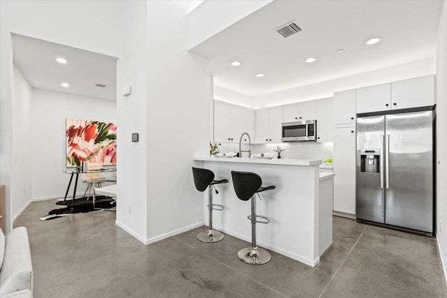 kitchen featuring kitchen peninsula, a breakfast bar area, stainless steel appliances, concrete floors, and white cabinets