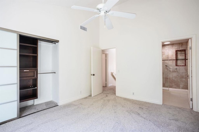 unfurnished bedroom featuring ceiling fan, a high ceiling, connected bathroom, light carpet, and a closet