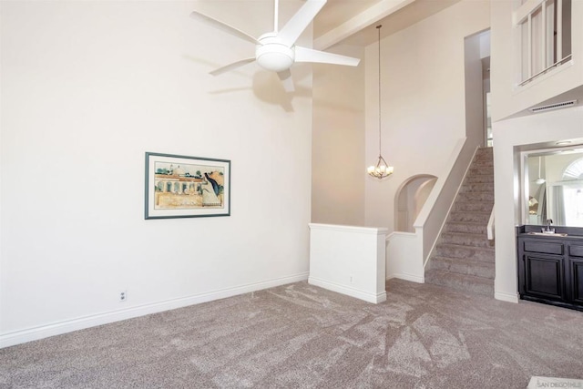 unfurnished living room with light carpet, sink, ceiling fan with notable chandelier, and beamed ceiling