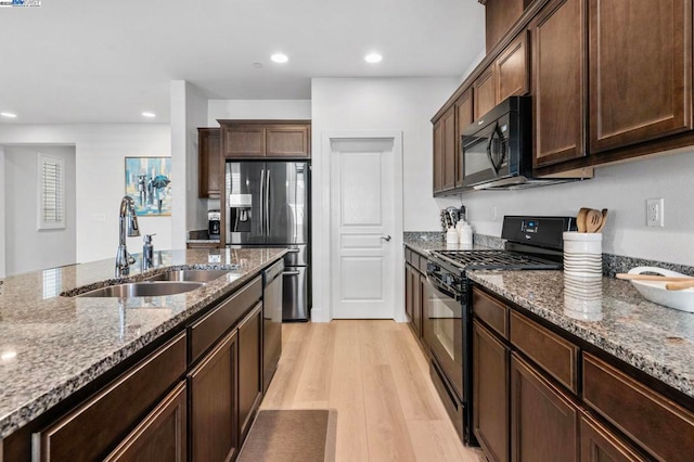 kitchen with dark brown cabinetry, light stone countertops, sink, black appliances, and light wood-type flooring