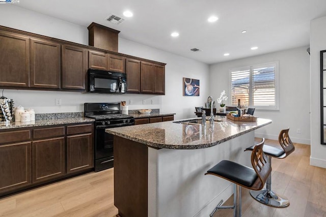 kitchen featuring sink, light wood-type flooring, dark stone countertops, and black appliances