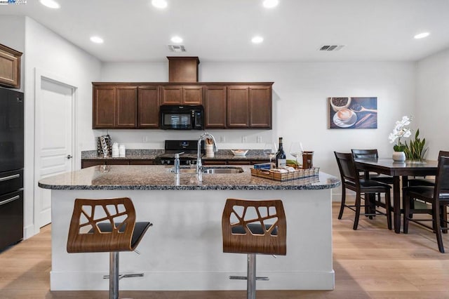 kitchen featuring black appliances, a kitchen breakfast bar, light wood-type flooring, and an island with sink