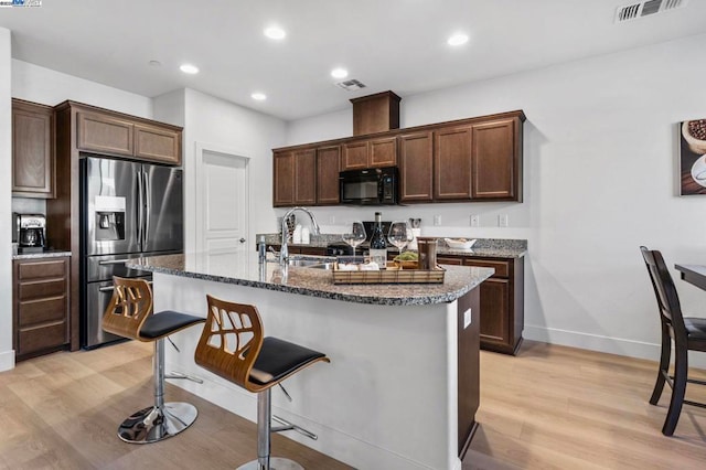 kitchen featuring a center island with sink, dark brown cabinetry, stainless steel fridge with ice dispenser, and light wood-type flooring