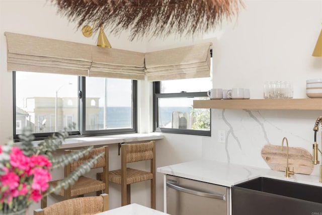 kitchen featuring tasteful backsplash, a sink, light stone counters, and stainless steel dishwasher