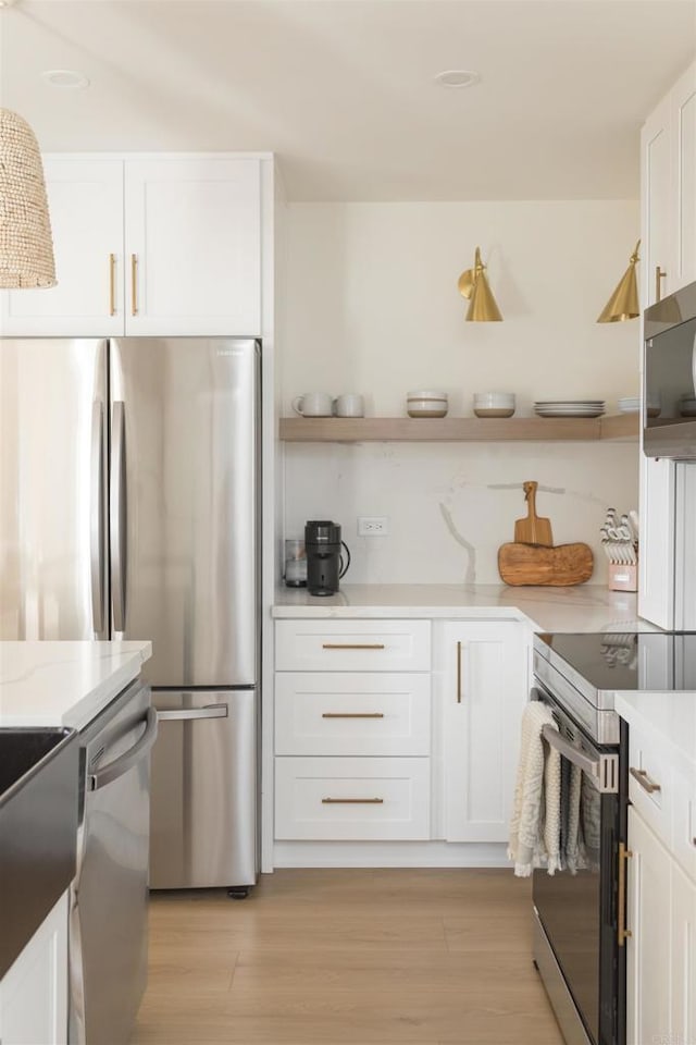 kitchen with light stone counters, open shelves, stainless steel appliances, light wood-style floors, and white cabinetry