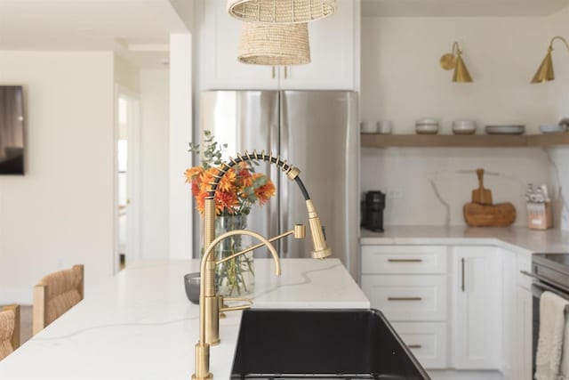 kitchen featuring stainless steel appliances, white cabinetry, a sink, and light stone countertops