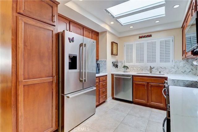 kitchen with a skylight, sink, decorative backsplash, light tile patterned floors, and appliances with stainless steel finishes