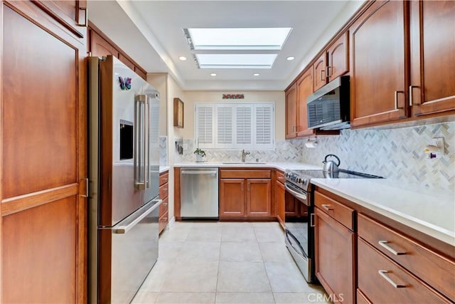 kitchen featuring backsplash, a skylight, stainless steel appliances, sink, and light tile patterned flooring