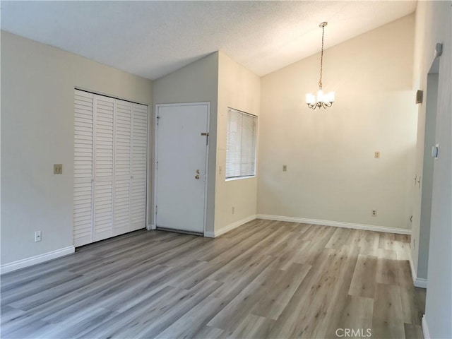 entryway with a notable chandelier, light hardwood / wood-style floors, a textured ceiling, and vaulted ceiling