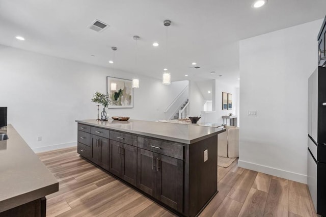 kitchen featuring decorative light fixtures, a center island with sink, light wood-type flooring, and dark brown cabinetry