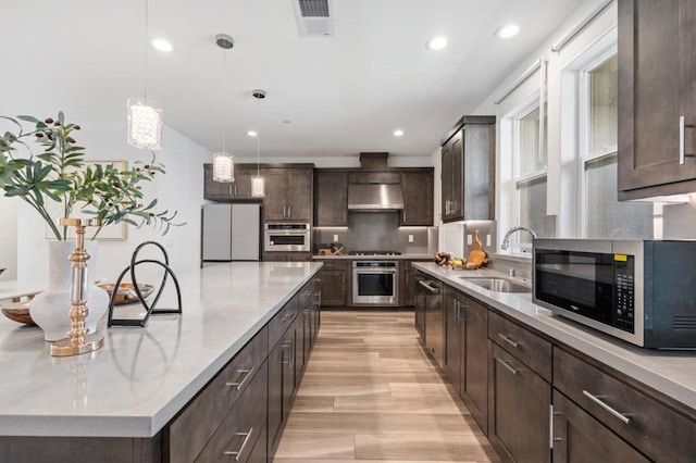 kitchen featuring hanging light fixtures, sink, light wood-type flooring, stainless steel appliances, and dark brown cabinetry