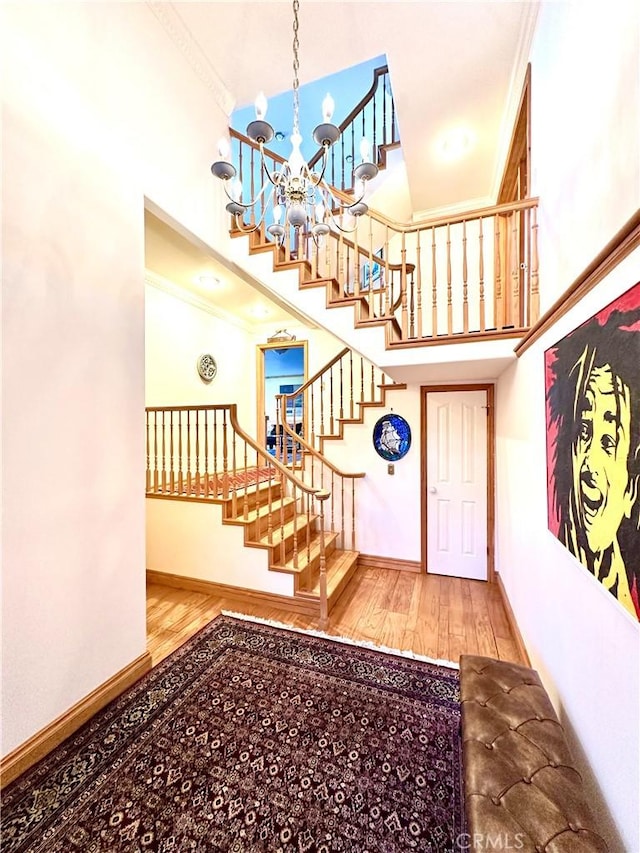 foyer entrance with a high ceiling, a notable chandelier, ornamental molding, and hardwood / wood-style floors