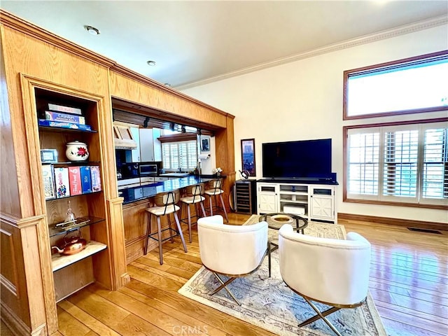 living room featuring plenty of natural light, ornamental molding, and light wood-type flooring