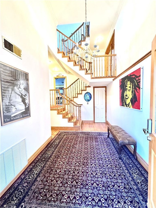 entrance foyer with hardwood / wood-style floors, crown molding, a high ceiling, and a chandelier