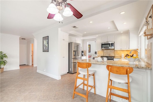 kitchen with kitchen peninsula, stainless steel appliances, a tray ceiling, white cabinets, and sink