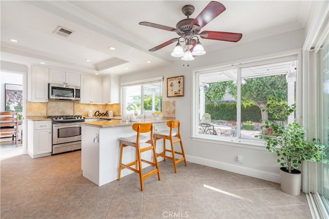 kitchen featuring a kitchen breakfast bar, appliances with stainless steel finishes, kitchen peninsula, a healthy amount of sunlight, and white cabinets