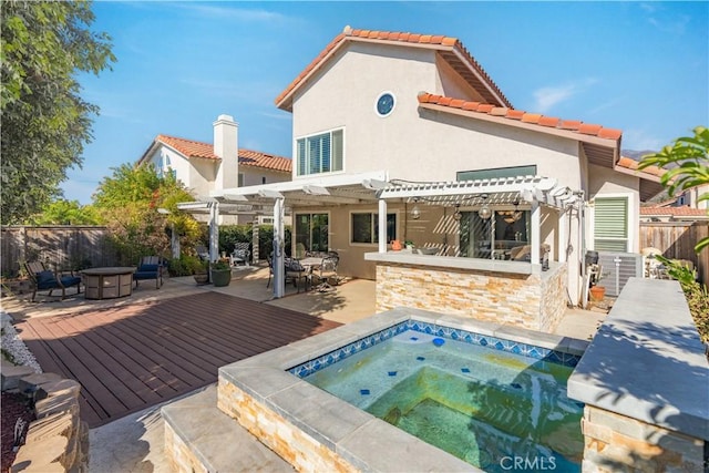 rear view of house with an in ground hot tub, a wooden deck, a fire pit, an outdoor bar, and a pergola