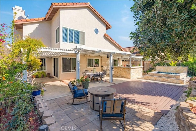 rear view of property featuring a wooden deck, an outdoor fire pit, a patio, and a pergola