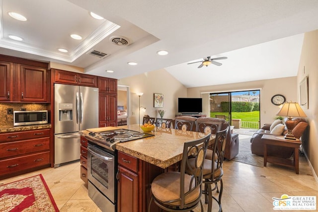 kitchen with a breakfast bar, a kitchen island, a tray ceiling, appliances with stainless steel finishes, and ceiling fan