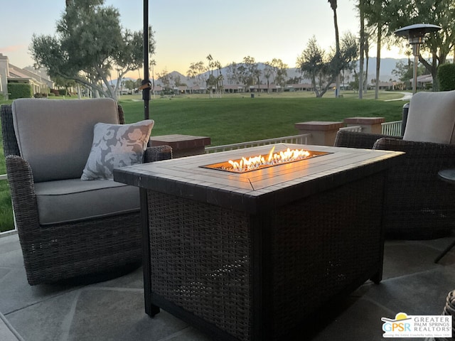 patio terrace at dusk featuring an outdoor fire pit and a lawn