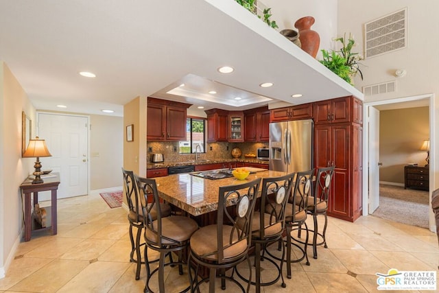 kitchen featuring sink, a raised ceiling, stainless steel refrigerator with ice dispenser, a kitchen island, and a breakfast bar