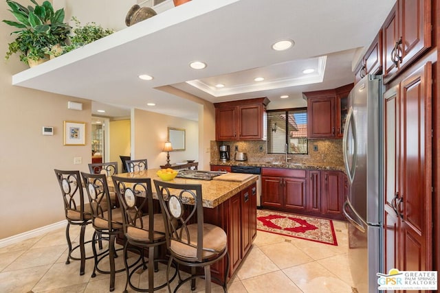 kitchen with a kitchen breakfast bar, a raised ceiling, stainless steel appliances, light stone countertops, and a kitchen island