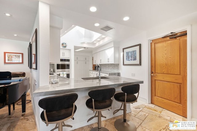 kitchen with sink, white cabinetry, tasteful backsplash, kitchen peninsula, and stainless steel double oven