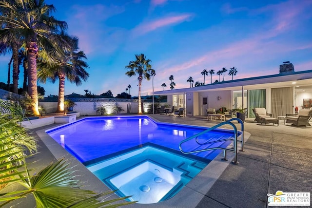 pool at dusk with an in ground hot tub and a patio area