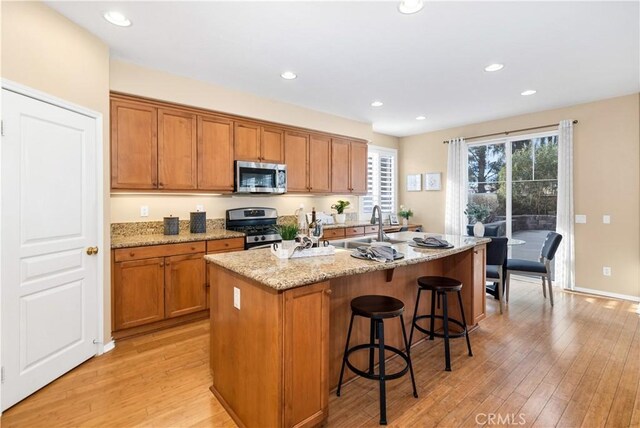 kitchen with light hardwood / wood-style floors, an island with sink, a breakfast bar area, stainless steel appliances, and light stone counters