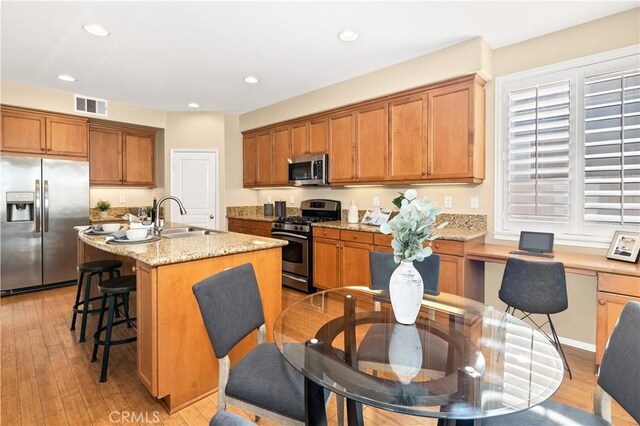 kitchen featuring sink, light hardwood / wood-style flooring, a kitchen island with sink, stainless steel appliances, and light stone counters