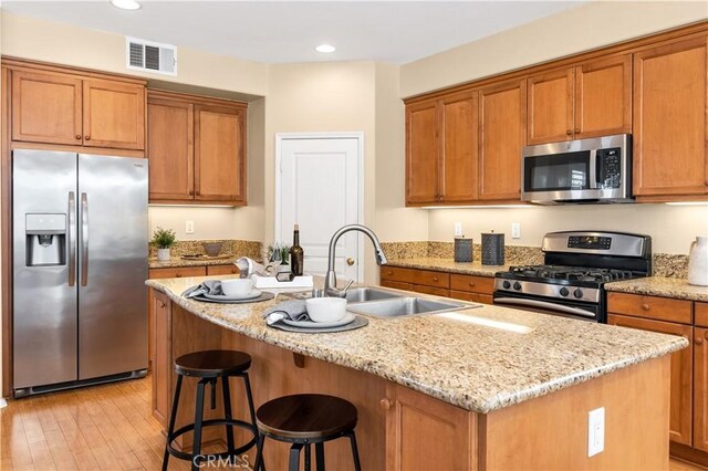 kitchen featuring light stone countertops, sink, appliances with stainless steel finishes, and a center island with sink