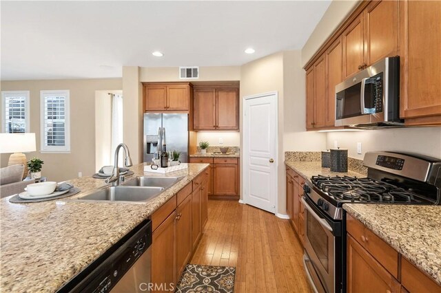 kitchen with light stone countertops, sink, light hardwood / wood-style flooring, and stainless steel appliances