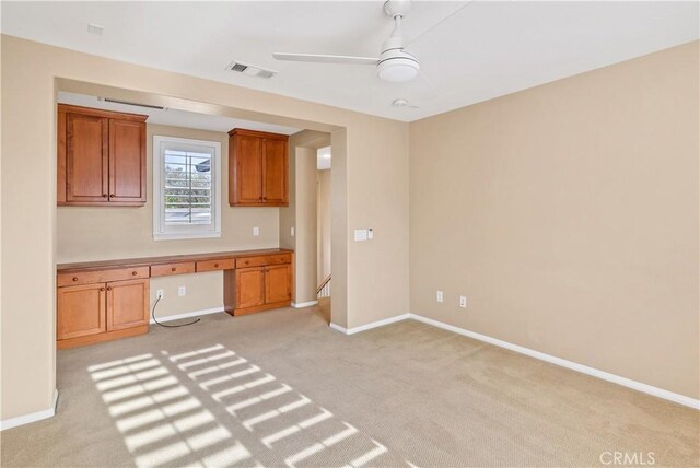 kitchen featuring ceiling fan, light carpet, and built in desk