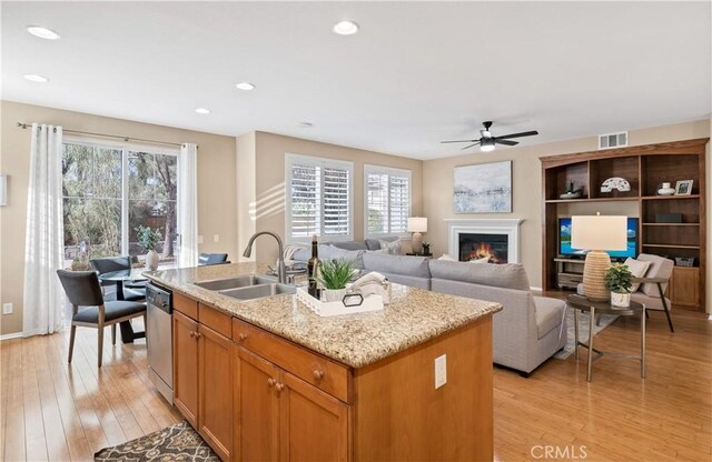 kitchen with dishwasher, an island with sink, sink, light wood-type flooring, and ceiling fan