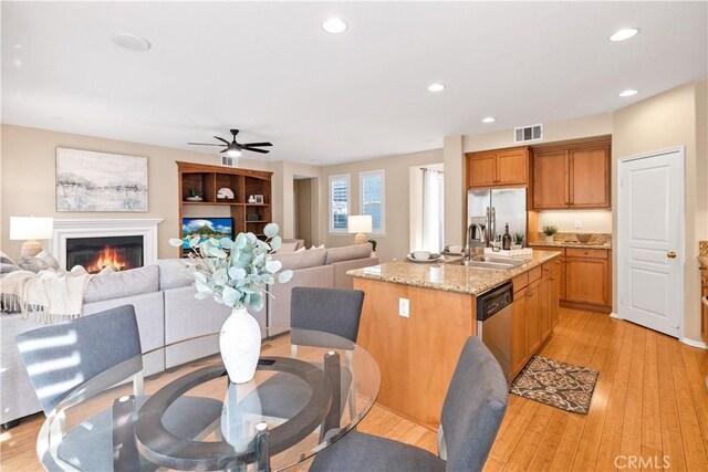 kitchen with stainless steel appliances, sink, a kitchen island with sink, light wood-type flooring, and ceiling fan