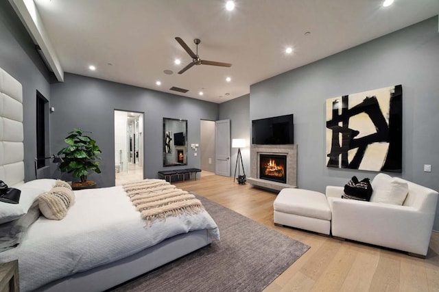 bedroom with ceiling fan, light wood-type flooring, and a tiled fireplace