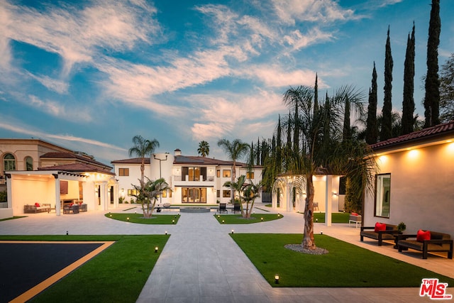 back house at dusk featuring an outdoor hangout area, a balcony, a patio, and a lawn