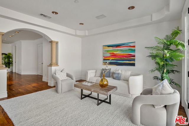 living room featuring decorative columns, a tray ceiling, and dark hardwood / wood-style flooring