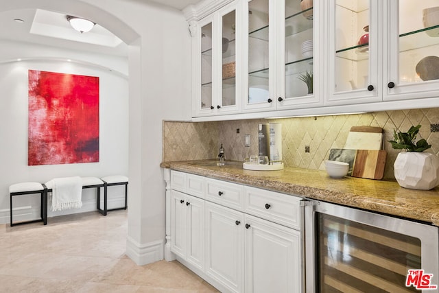 bar featuring beverage cooler, white cabinetry, light stone counters, and decorative backsplash