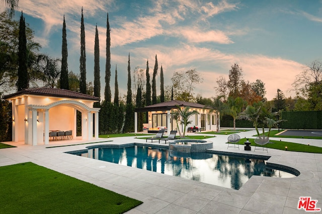 pool at dusk featuring a patio, an in ground hot tub, and an outdoor structure