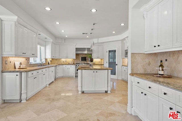 kitchen featuring a center island with sink, hanging light fixtures, stainless steel appliances, light stone countertops, and white cabinets