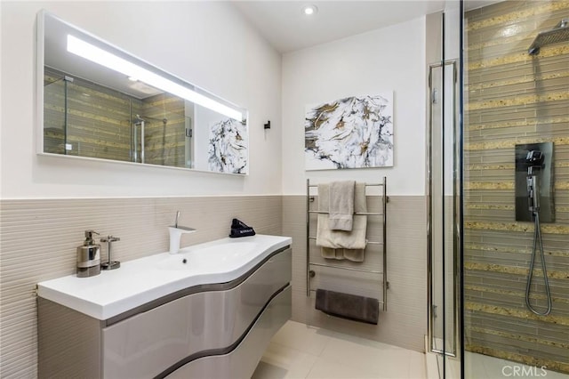 bathroom with tile walls, tile patterned flooring, a shower, and vanity