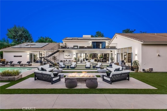 rear view of property with an outdoor living space with a fire pit, a balcony, a patio, and solar panels