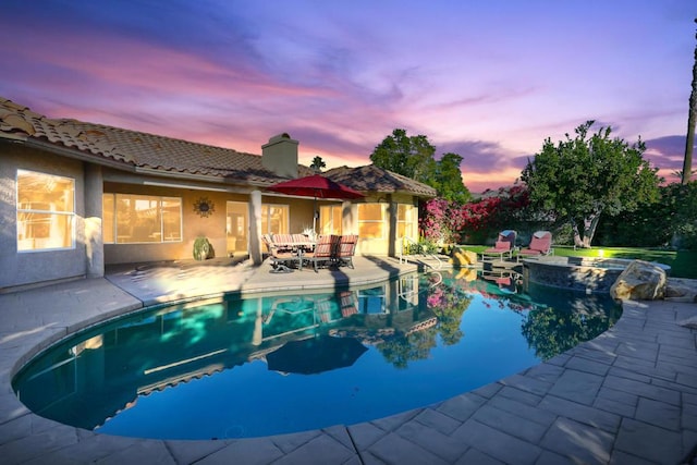 pool at dusk featuring an in ground hot tub and a patio