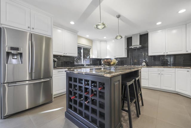 kitchen featuring wall chimney range hood, stainless steel refrigerator with ice dispenser, and white cabinetry